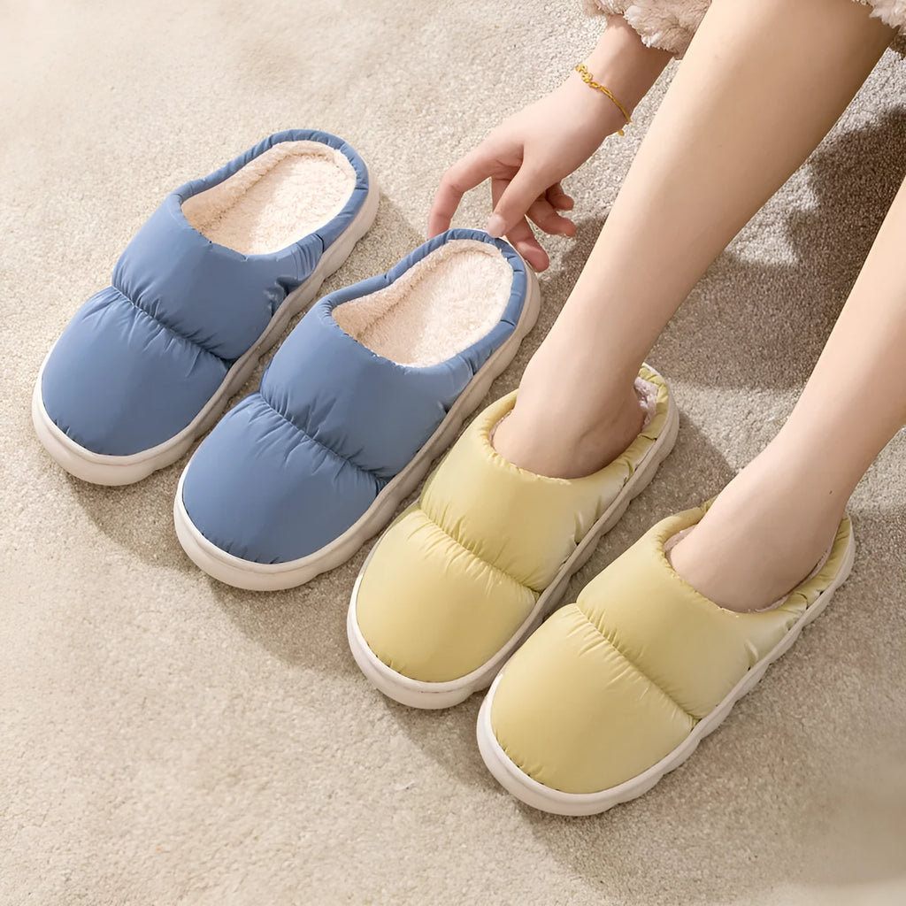 Pair of thick-soled indoor slippers in blue with a wrapped toe, low heel, and artificial plush lining.