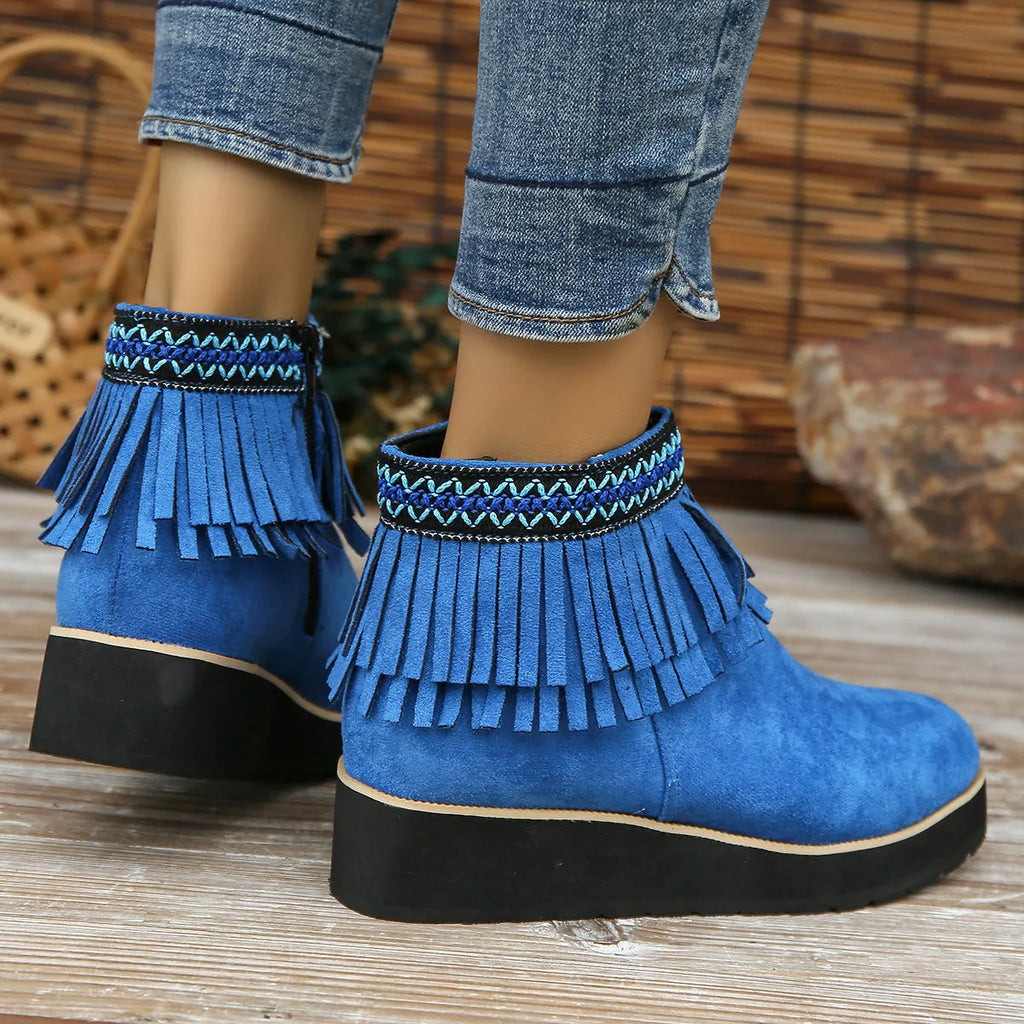 Women's suede ankle boots with a wedge heel, side zipper, tassel detail, and thick rubber sole.