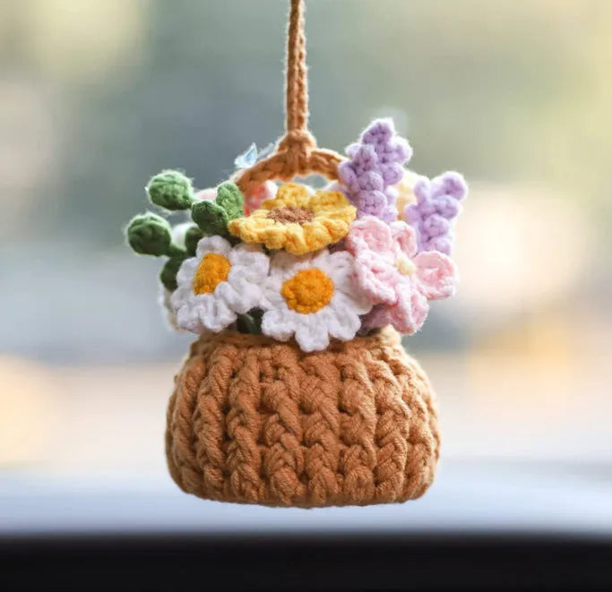 Green and white knitted wool car plant decoration with hanging rope on a car dashboard.