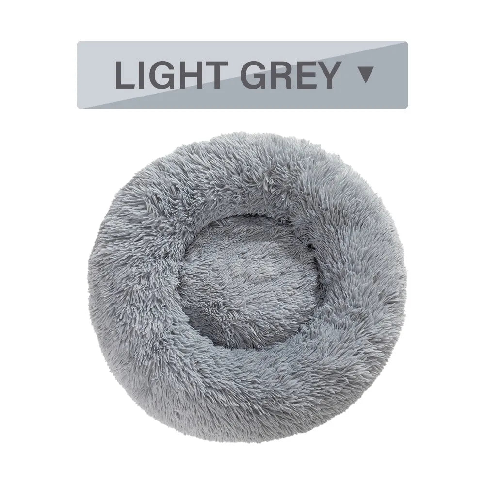 Fluffy donut-shaped dog bed in long plush material, shown in a light grey colour.
