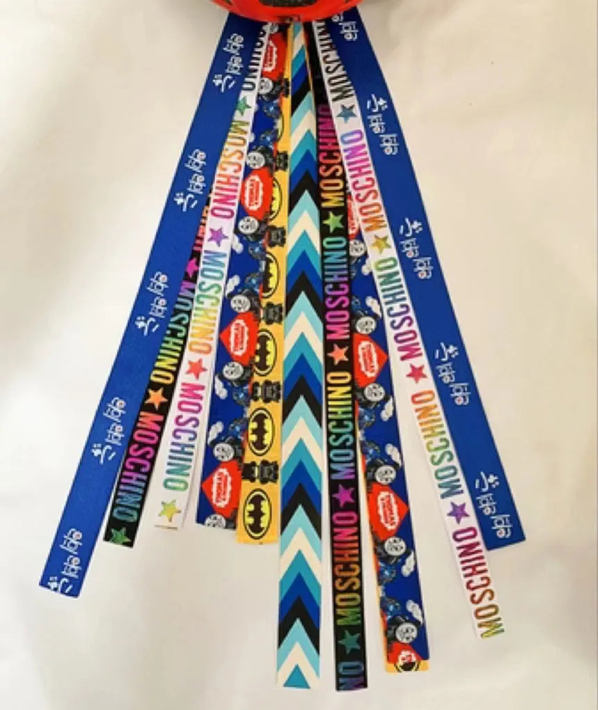 Colourful fabric helmet streamers for children's roller skating and ski helmets, shown in apricot, red, and grey.