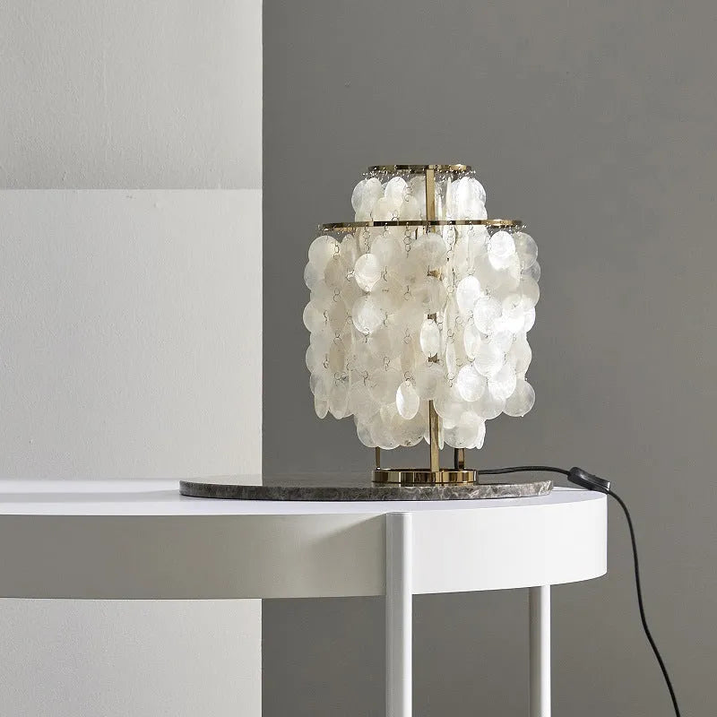 Modern bedside table lamp with a decorative white shell-shaped shade on a metallic chrome or gold base.