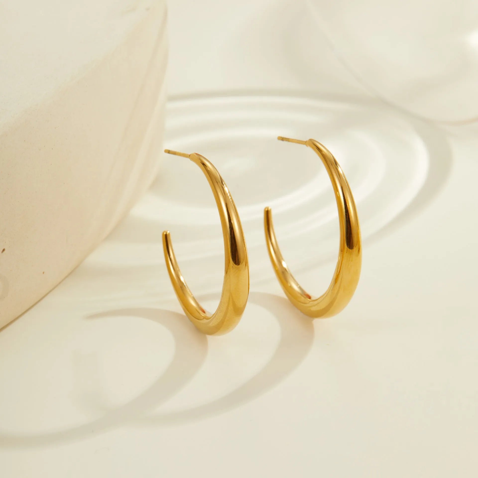 A pair of simple round titanium stainless steel hoop earrings shown in both gold and steel finishes.