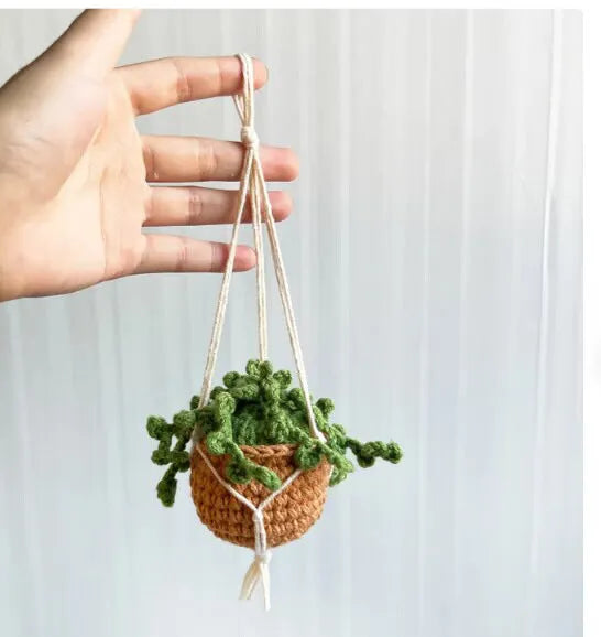 Green and white knitted wool car plant decoration with hanging rope on a car dashboard.