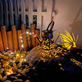 Tapered iron solar garden lantern with butterfly pattern emitting warm white light.