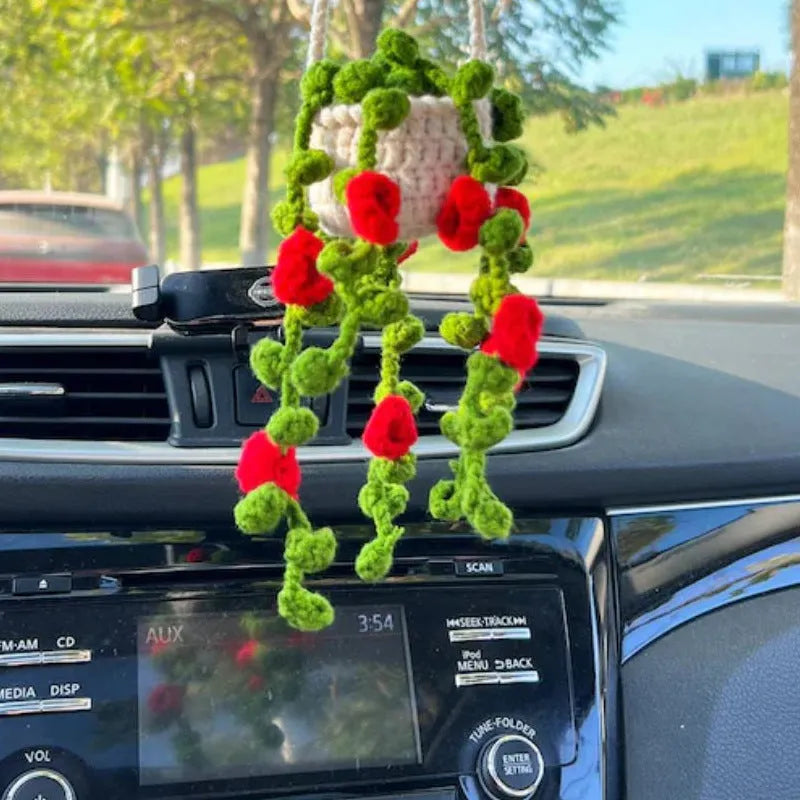 Green and white knitted wool car plant decoration with hanging rope on a car dashboard.