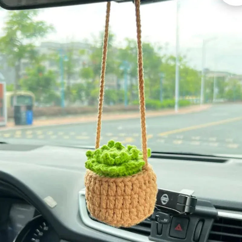 Green and white knitted wool car plant decoration with hanging rope on a car dashboard.