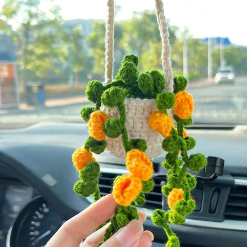 Green and white knitted wool car plant decoration with hanging rope on a car dashboard.
