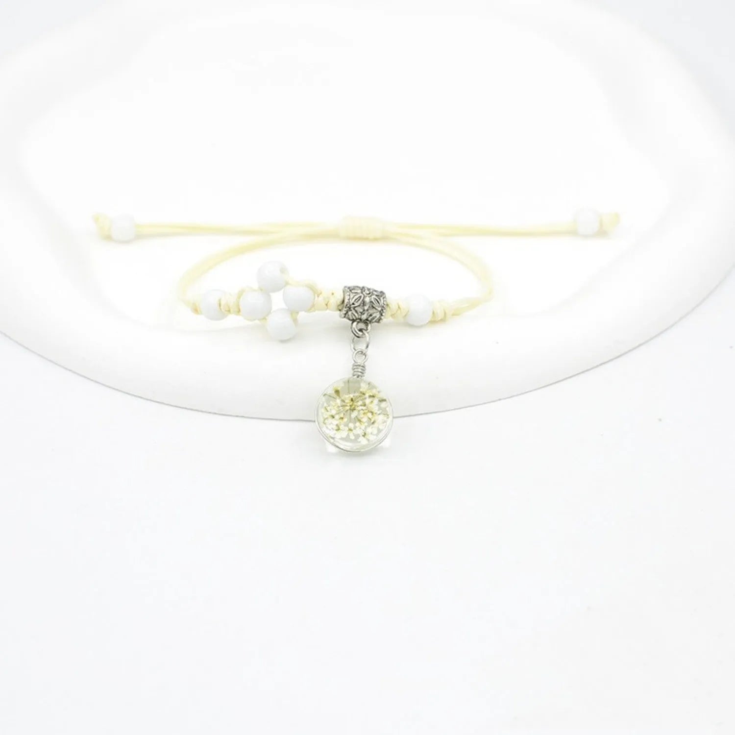Close-up of a hand-woven glass bracelet with large beads containing real dried flowers and a lace design.