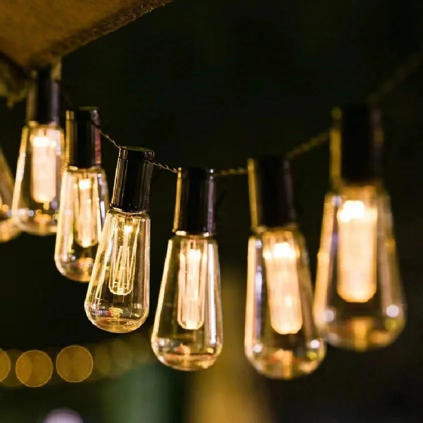 Waterproof outdoor string lights with retro glass bottle-shaped lamps hanging from a green wire.
