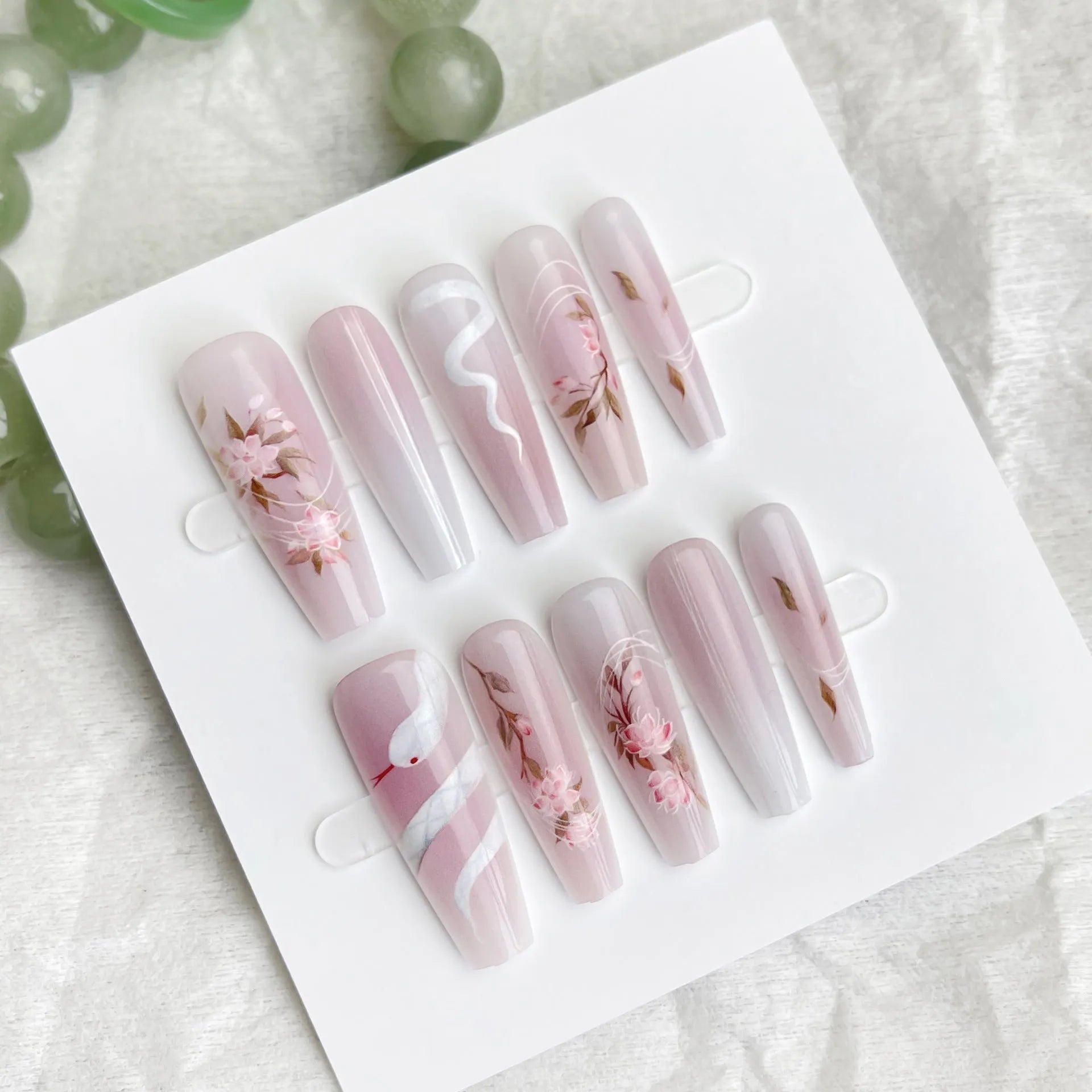 Ancient Chinese style snake year red prefabricated nail tips in drunk flower colour, long ladder shape, on a display stand