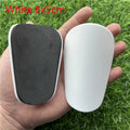 Extra small black and white plastic football shin guards for junior players, shown at 8x5 cm size.