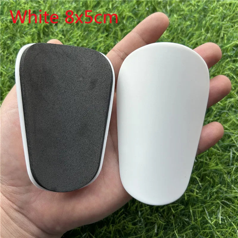 Extra small black and white plastic football shin guards for junior players, shown at 8x5 cm size.