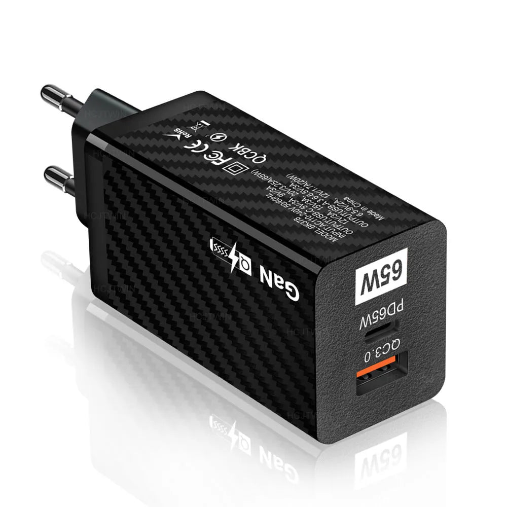 Compact black 65W GaN USB-C laptop charger with UK plug next to laptop