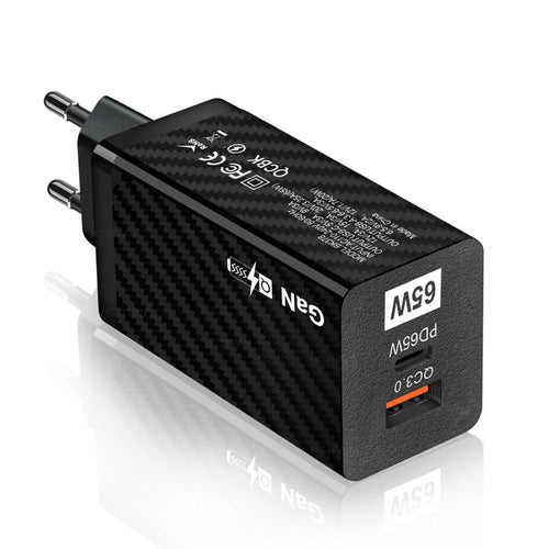 Compact black 65W GaN USB-C laptop charger with UK plug next to laptop