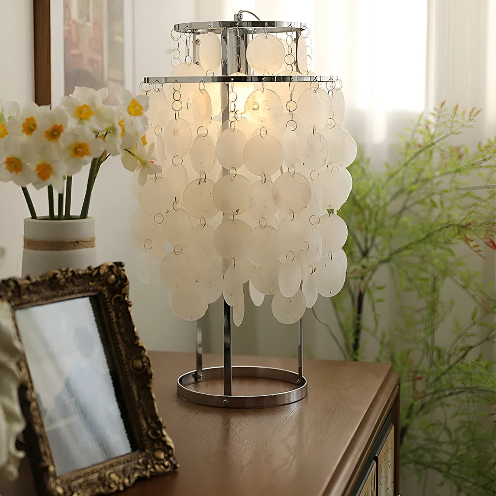 Modern bedside table lamp with a decorative white shell-shaped shade on a metallic chrome or gold base.