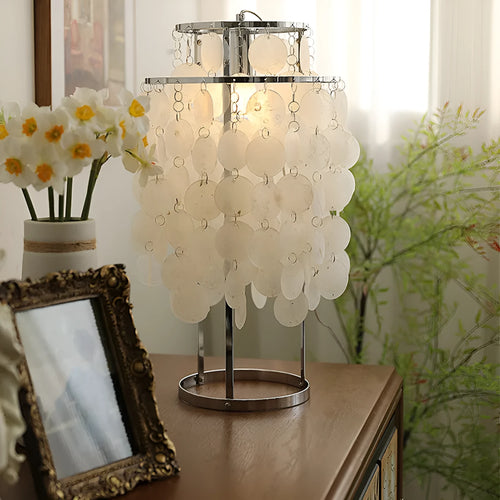 Modern bedside table lamp with a decorative white shell-shaped shade on a metallic chrome or gold base.
