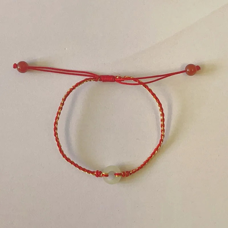 Red rope braided bracelet with natural wave-shaped Hetian jade pendant for Tiger Year birth year, on a neutral background