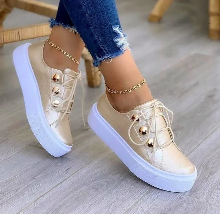Women's white lace-up flats sneakers with decorative silver rivets on the sides.