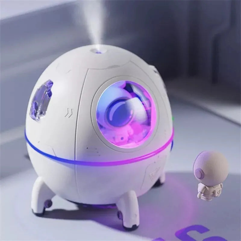Purple astronaut-themed desktop USB humidifier with LED light next to USB cable on a desk.