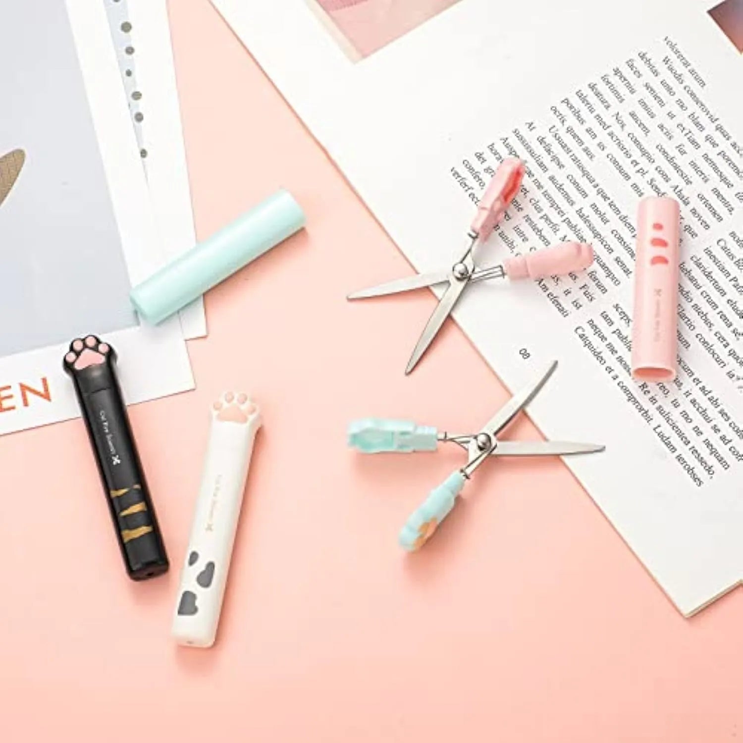 Small stainless steel folding scissors with cat paw handles shown in pink, blue, black, and white.