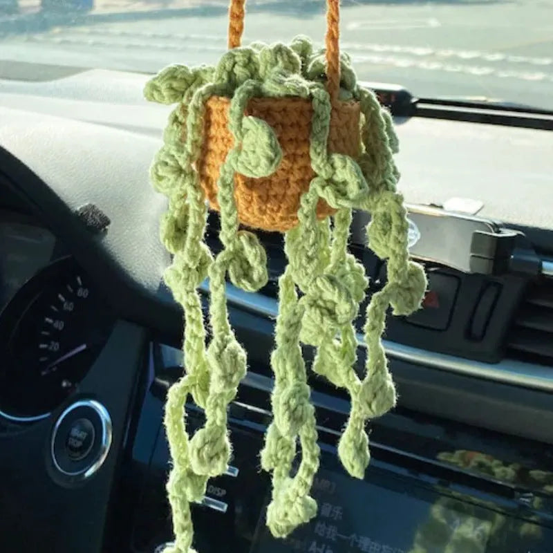 Green and white knitted wool car plant decoration with hanging rope on a car dashboard.