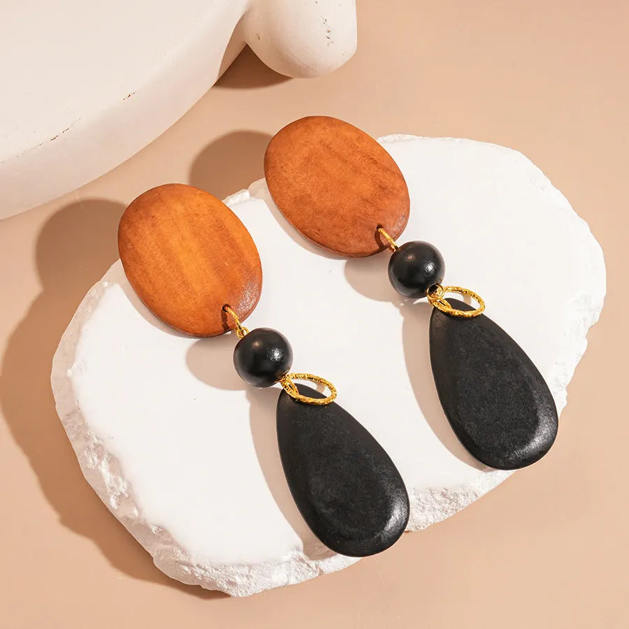 Close-up of handmade wooden elliptical earrings in silver, brown, and black colours on a retro-style background.