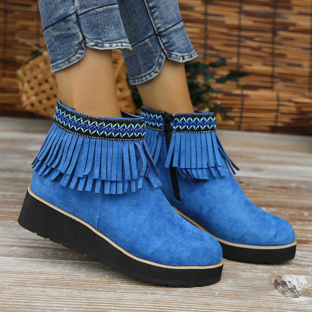 Women's suede ankle boots with a wedge heel, side zipper, tassel detail, and thick rubber sole.