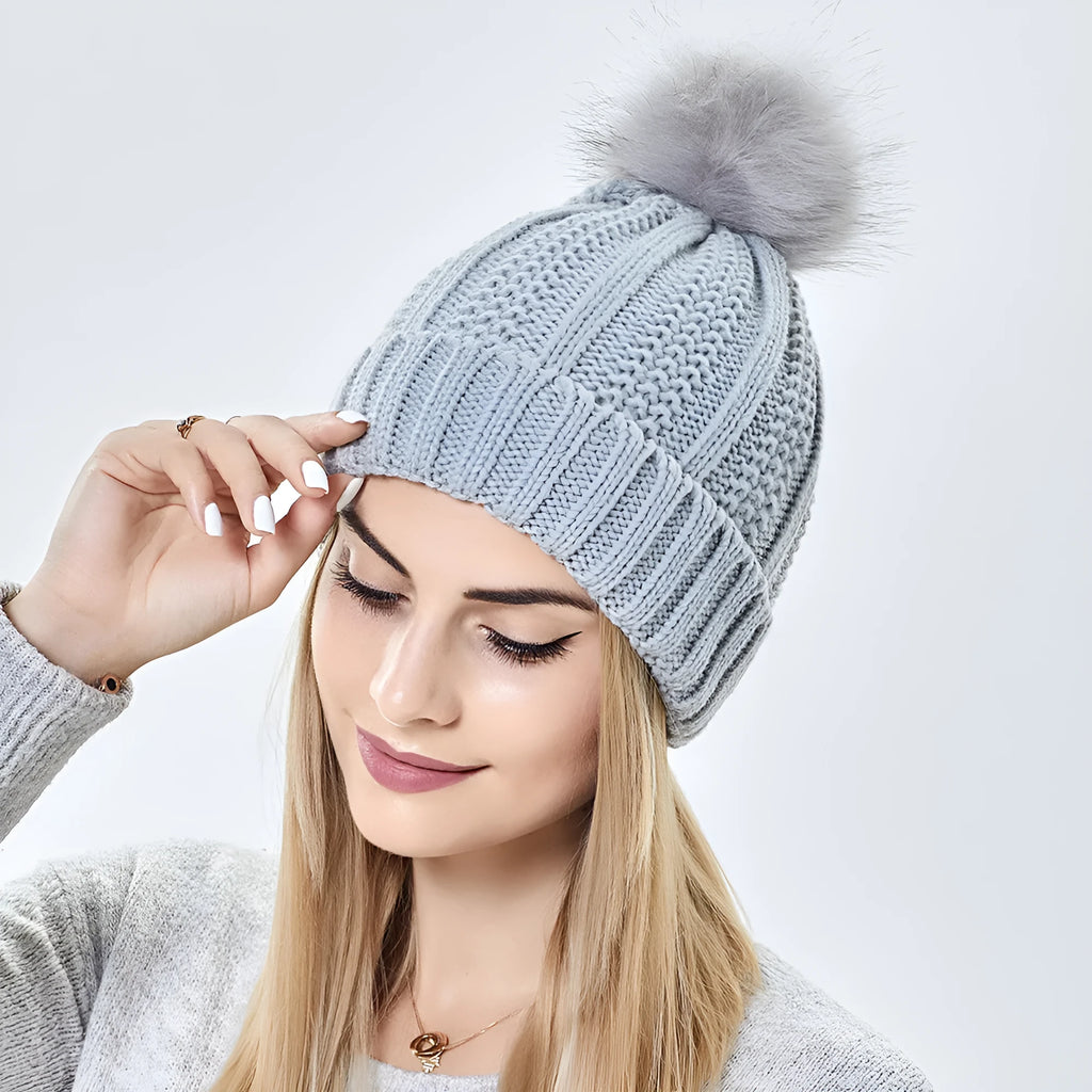 Women's knitted beanie hat with faux fur pom pom, shown in wine red, featuring a satin-lined interior.