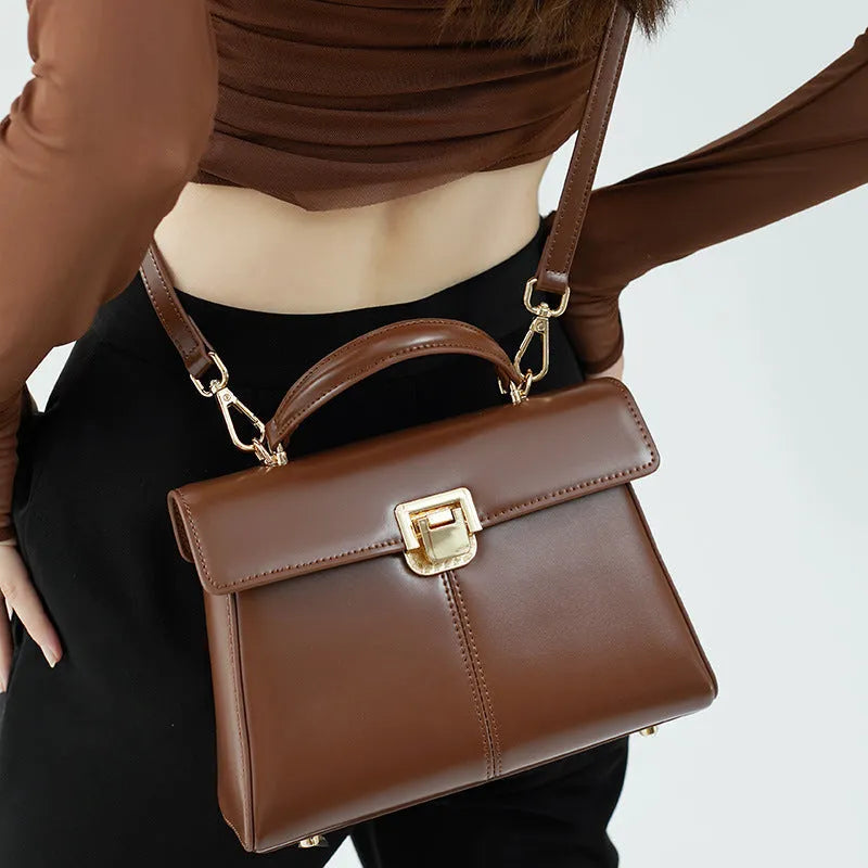 Women's black leather shoulder bag with vachette clasp, showing horizontal square shape and adjustable strap