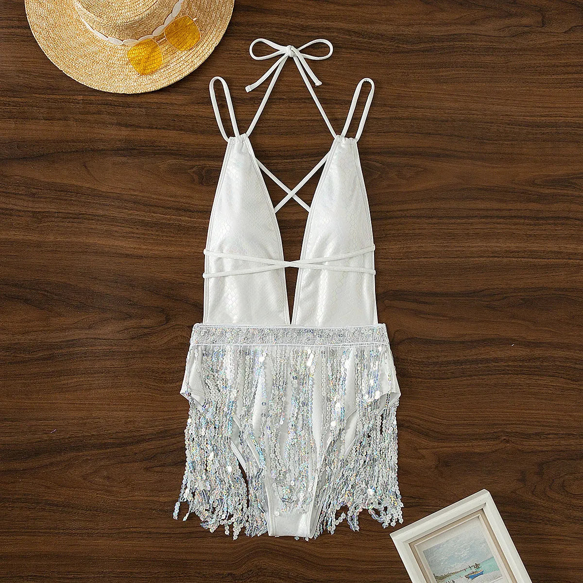 White one-piece swimsuit with deep V-neckline and tassel detail on a brief-cut, sleeveless design.