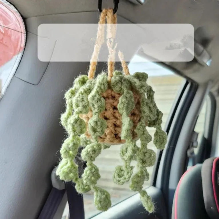 Green and white knitted wool car plant decoration with hanging rope on a car dashboard.