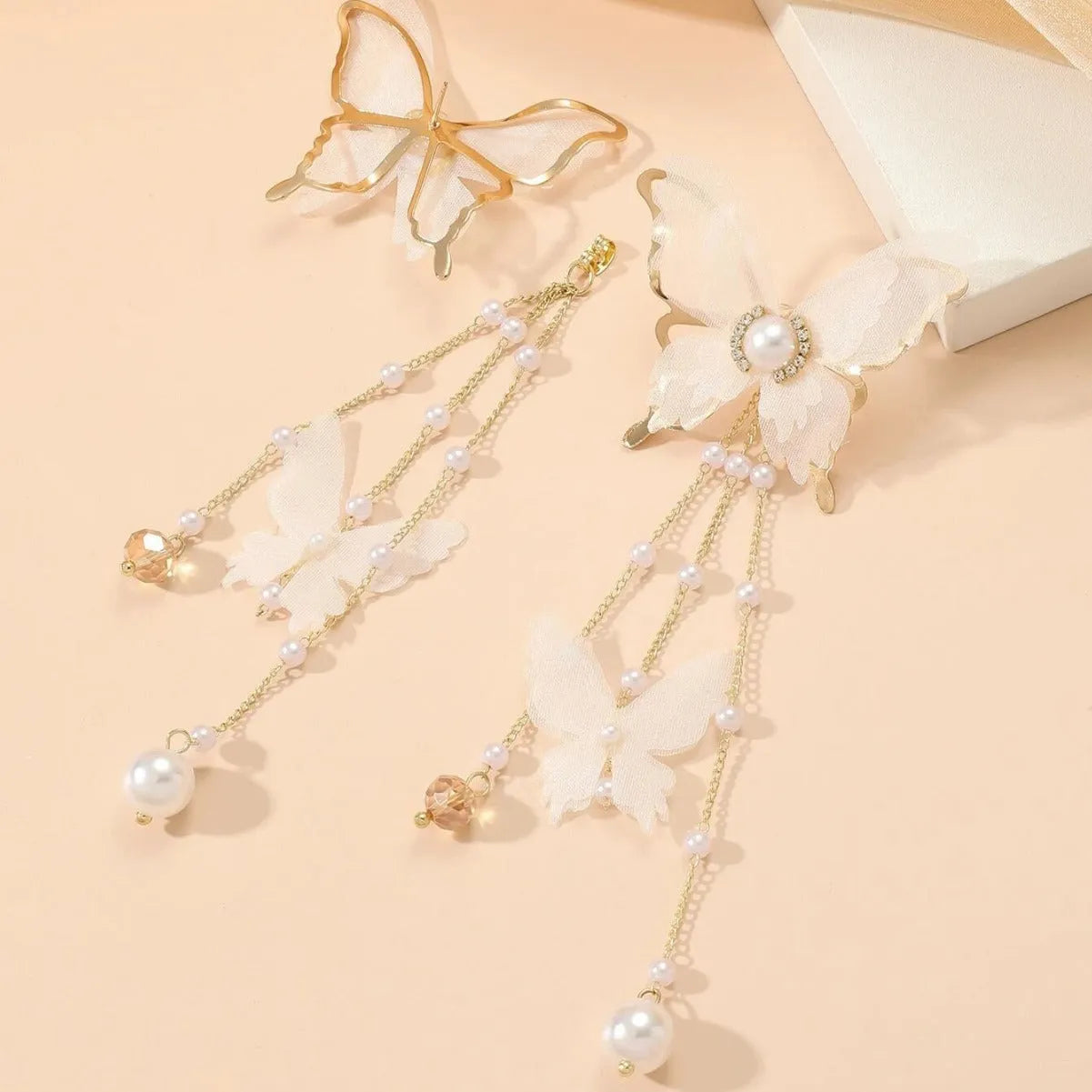 A pair of white butterfly-shaped earrings with pearls, rhinestones, and a dangling lace tassel.