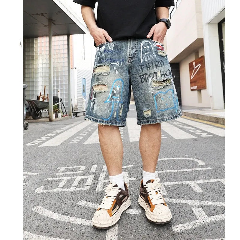 Blue men's ripped denim shorts with graffiti detailing and a straight-leg cut, showing front zipper fly.