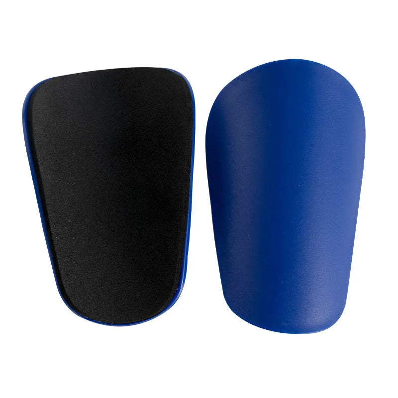 Two pairs of PU mini shin guards in black, white, red, and dream blue colours on a sports field.