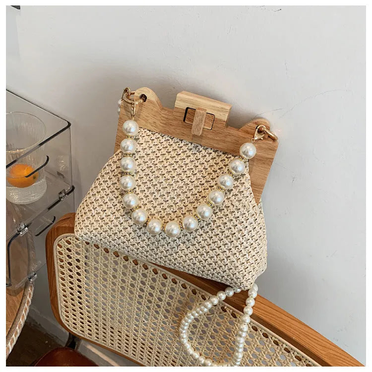 Women's woven straw shoulder bag with pearl chain detailing in horizontal square shape showing internal compartments