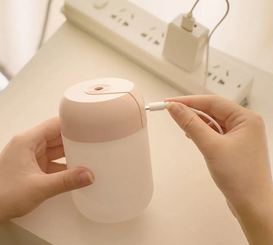 White cylindrical USB mini humidifier on desk with charging cable