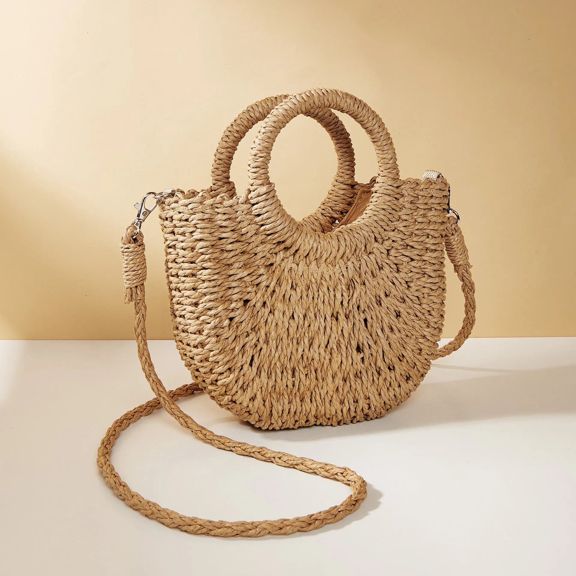 Woven straw beach bag in beige, peach skin lining, crossbody style, 24cm height, on a sandy beach