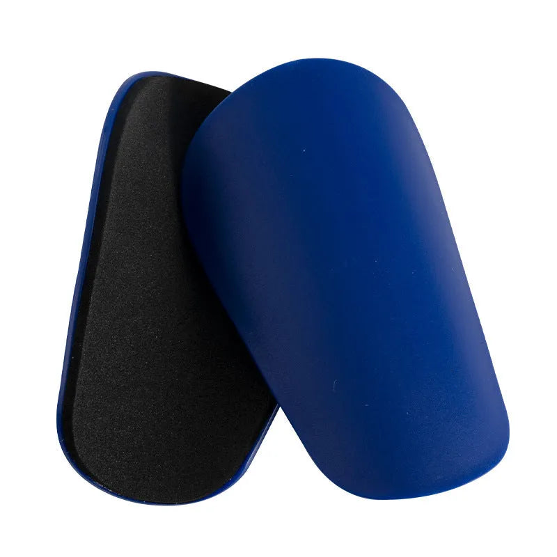 Two pairs of PU mini shin guards in black, white, red, and dream blue colours on a sports field.