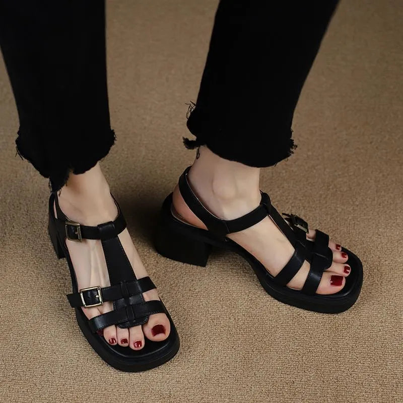 Women's black retro sandals with T-shaped buckle, chunky heel, and square open toe on a plain background.