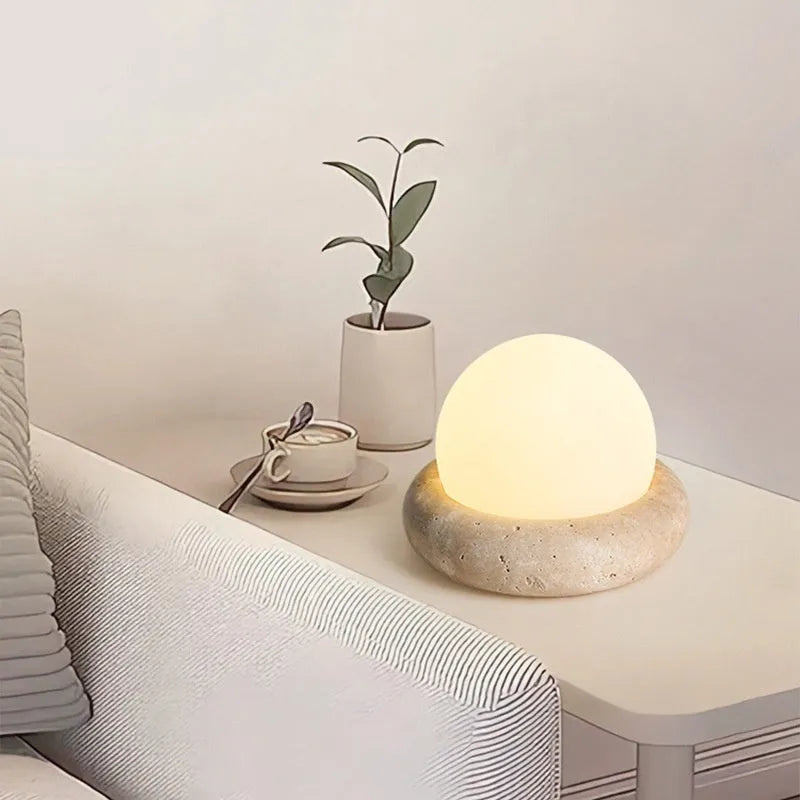 Cream coloured round rechargeable remote control night light on a bedside table.