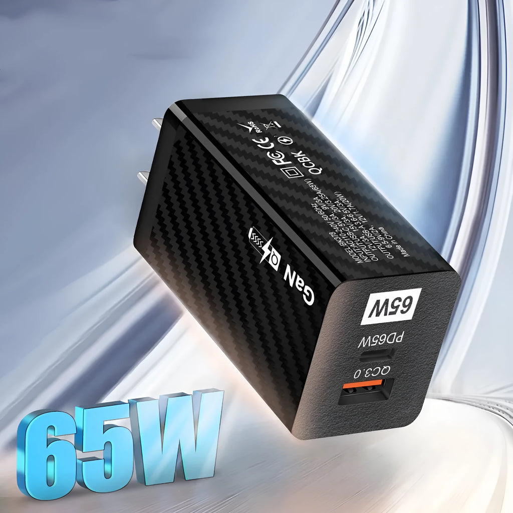 Compact black 65W GaN USB-C laptop charger with UK plug next to laptop