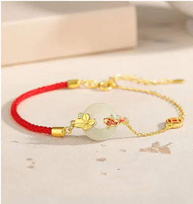 Women's silver bracelet with gold peace buckle and koi fish charm on a red rope.