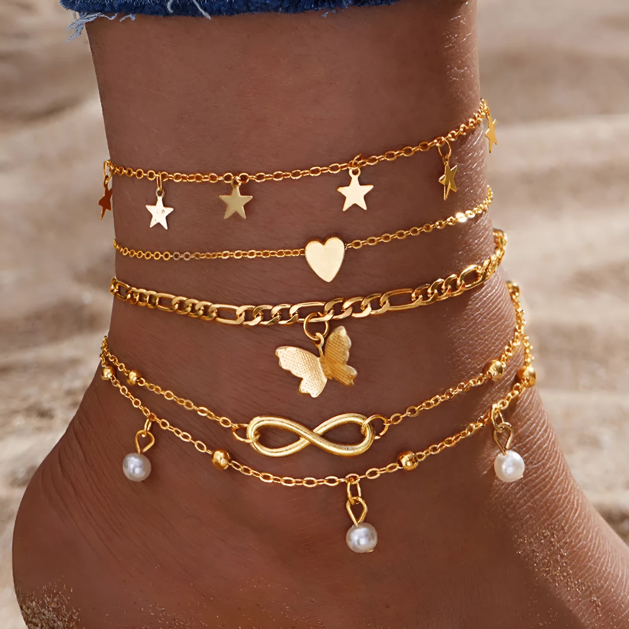 Four gold-tone alloy anklets with butterfly and heart pearl charms arranged as a set