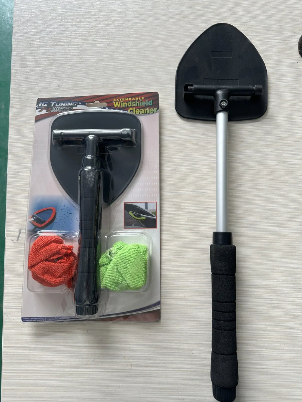 A plastic car windscreen cleaning brush with a long handle, shown in red, green, and blue colour options.