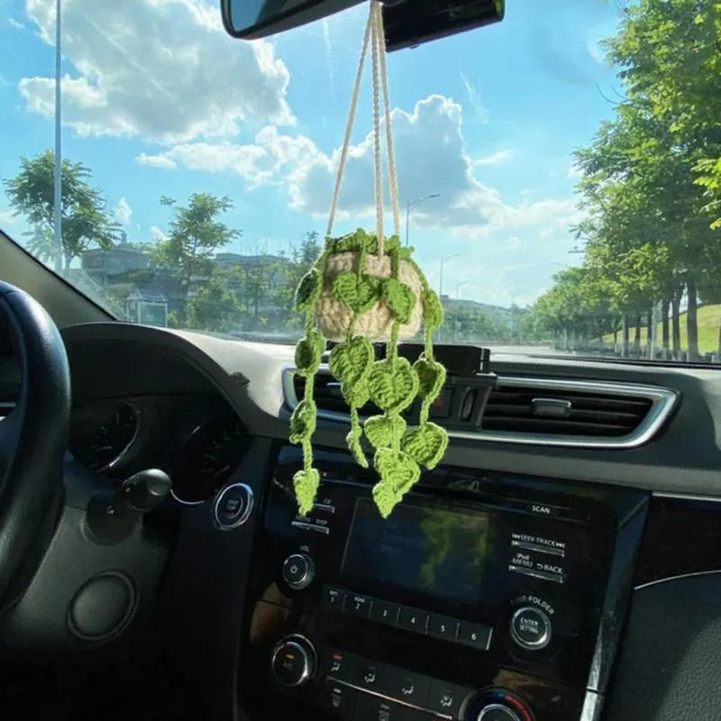 Green and white knitted wool car plant decoration with hanging rope on a car dashboard.