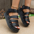 Thick-soled black buckle strap sandals on a beach, showing PU upper and rubber sole.