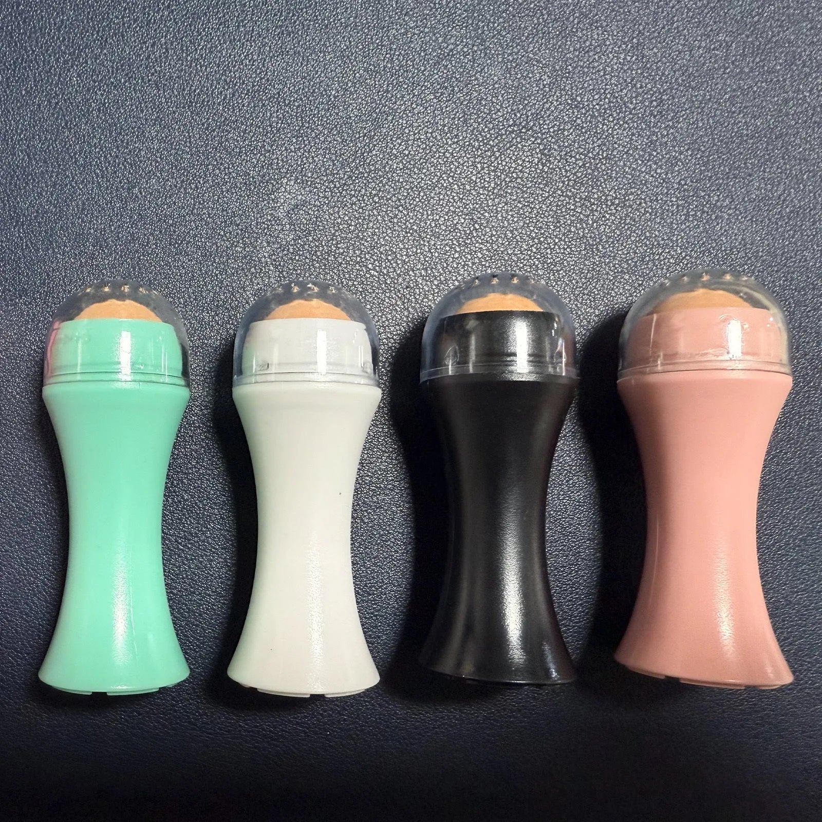 Portable black volcanic stone roller for oily skin control on a pink background.