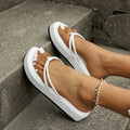 White thick-soled flip-flops with herringbone pattern PU upper and rubber sole on a sandy beach.