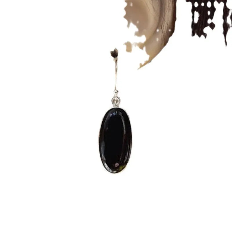 Oval black agate stone set in a geometric silver electroplated frame, forming a drop pendant earring for women.